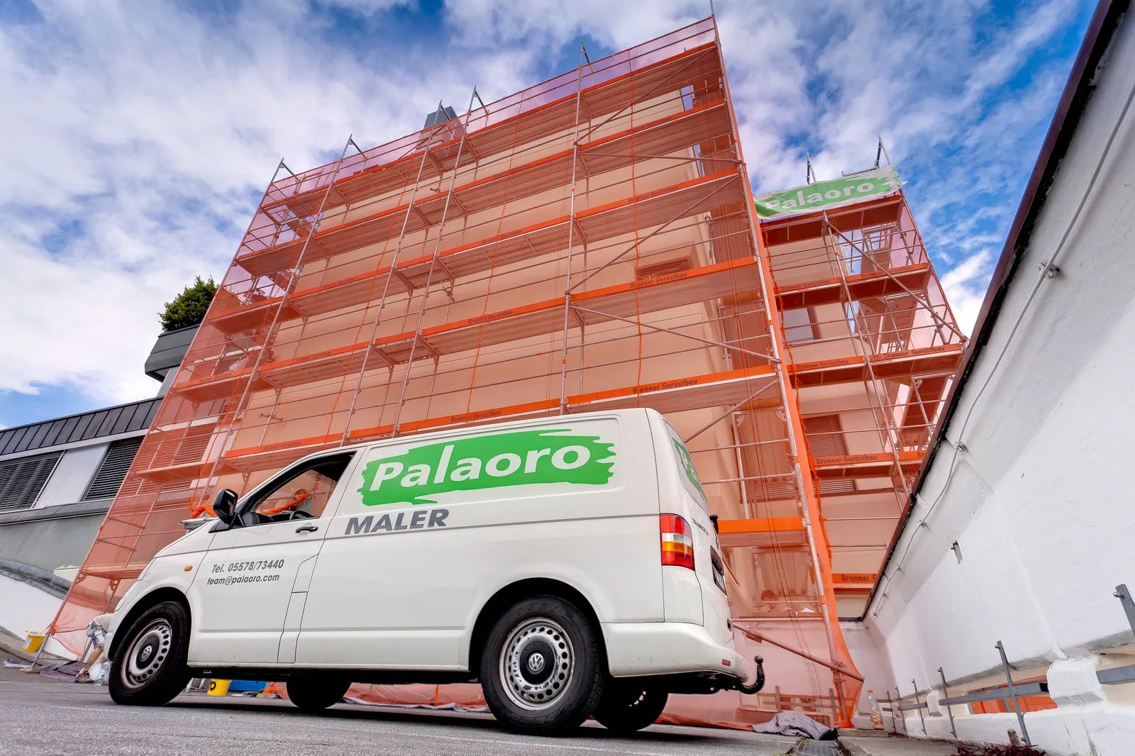 Firmenwagen von Palaoro vor einem komplett eingerüsteten Haus, am Gerüst hängt ein Palaoro-Banner